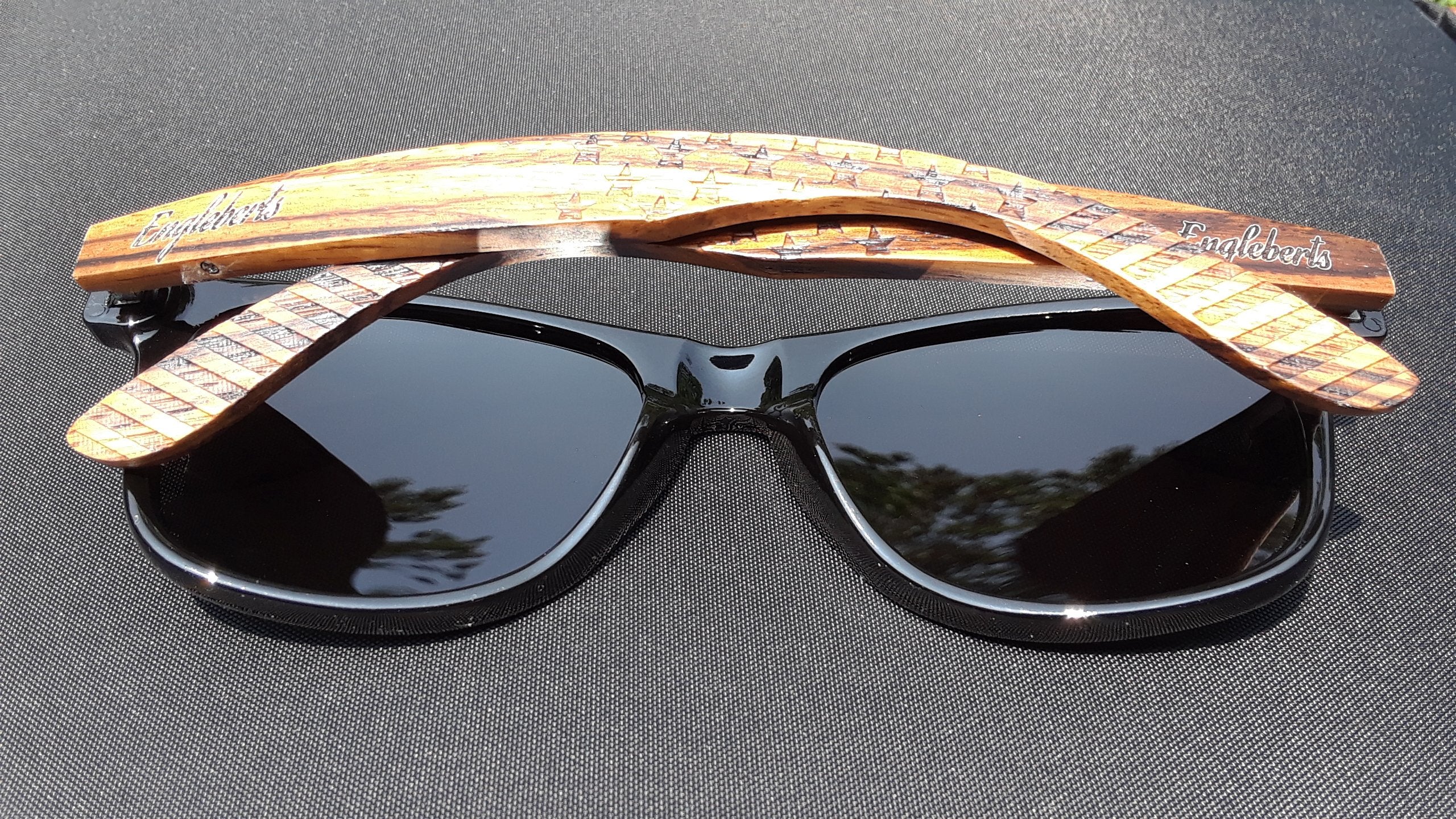 Black sunglasses with wooden, engraved arms on a dark surface.