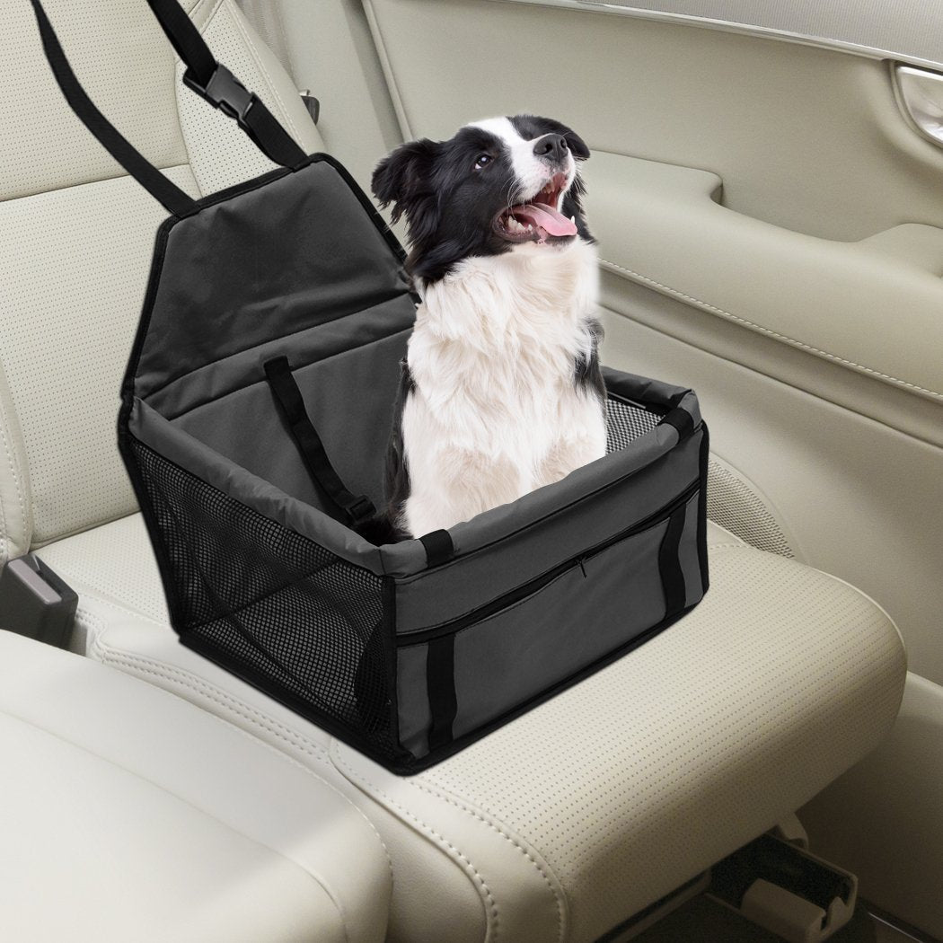 Dog in a black pet car seat with beige interior, looking up and panting.
