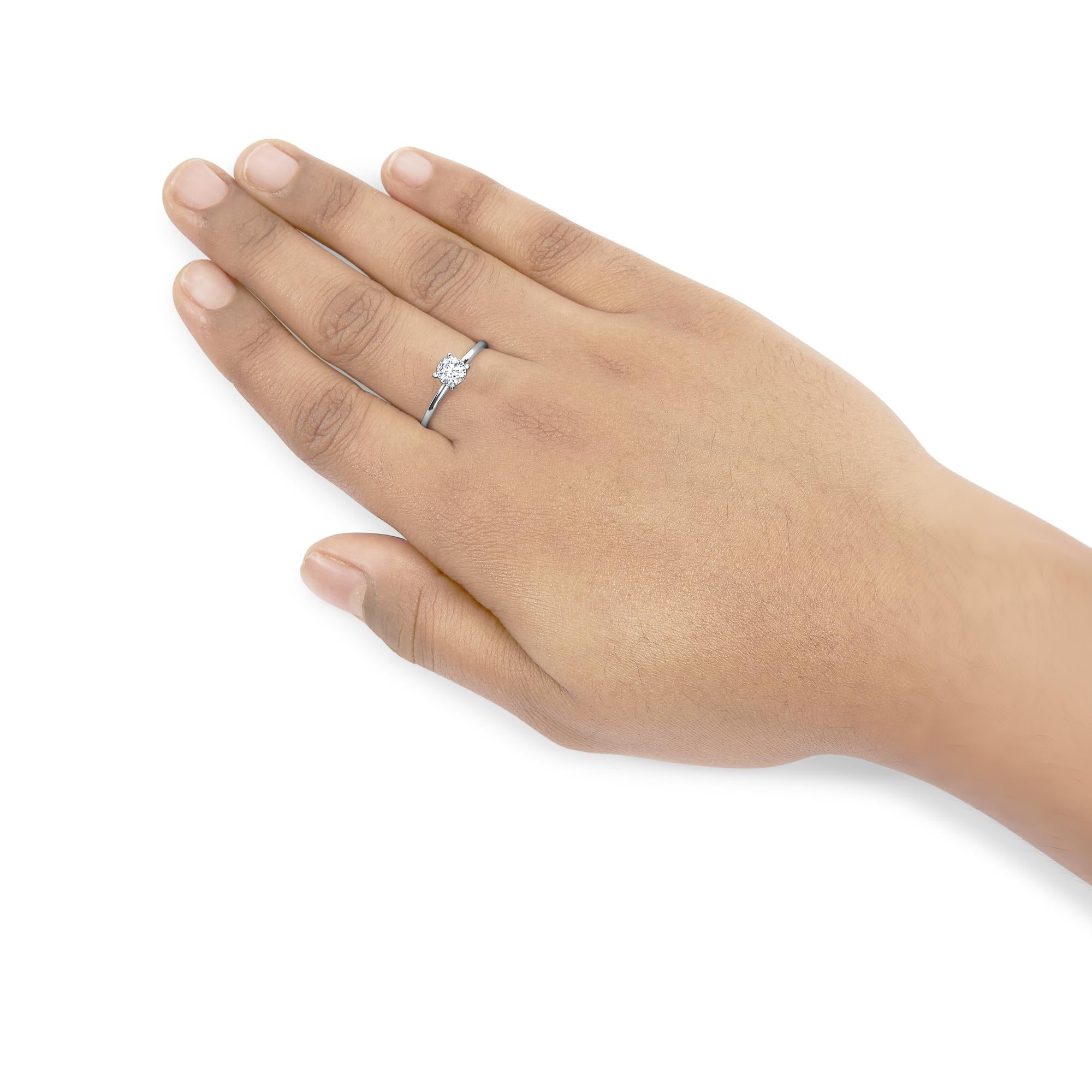 Hand wearing a silver ring with a round diamond, set against a white background.