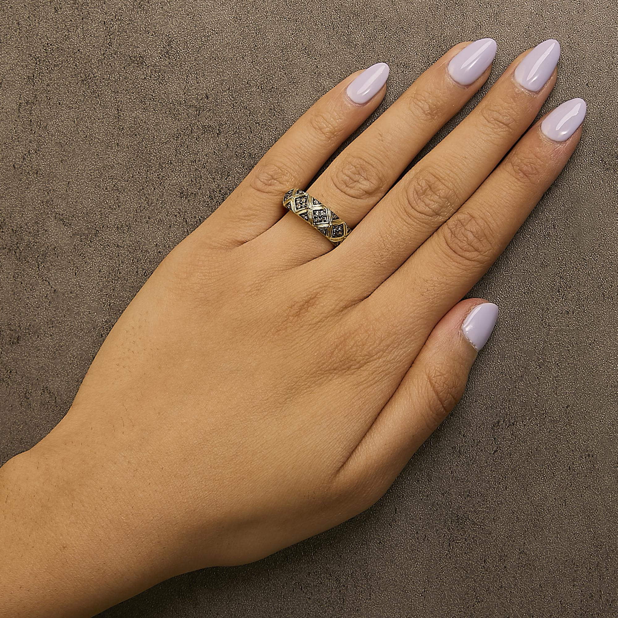 Hand with lilac nails wearing a gold and black patterned ring on a textured gray surface.