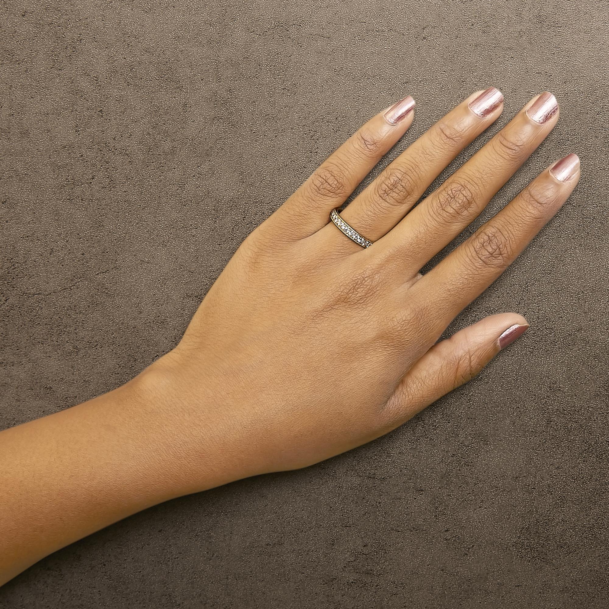Hand with pink nails wearing a diamond ring on ring finger against a textured gray background.