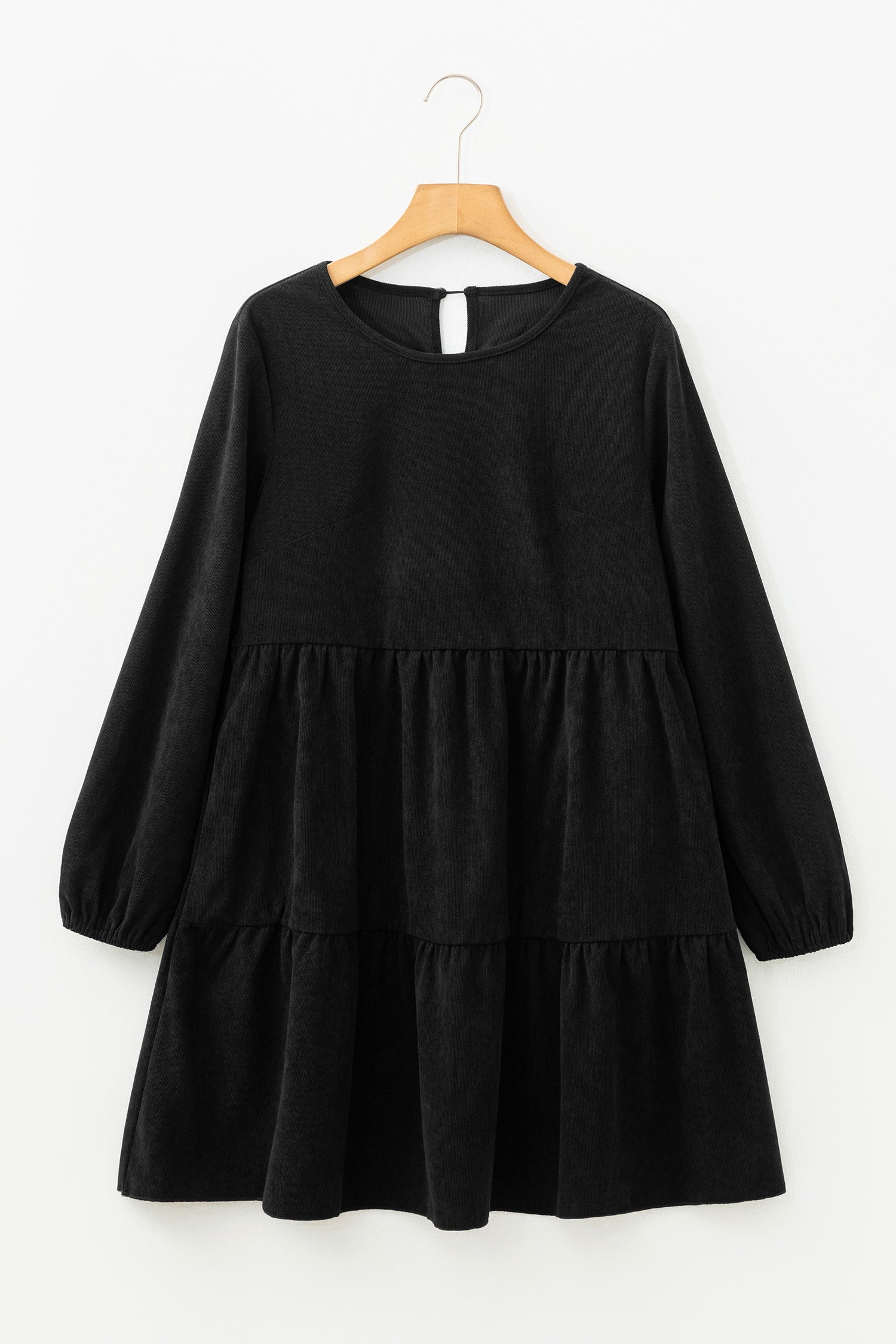 Black, long-sleeved, tiered dress on a wooden hanger against a white background.