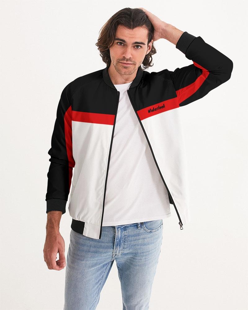 Man in a black, white, and red jacket, wearing light blue jeans, poses hand in hair.