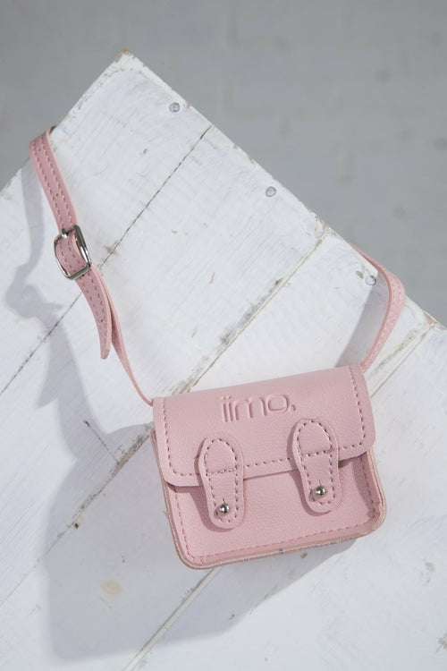 Small pink leather bag with buckle details on a white wooden surface.