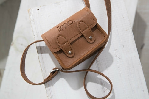 Small brown leather satchel with double buckles and a strap, on a white wooden surface.