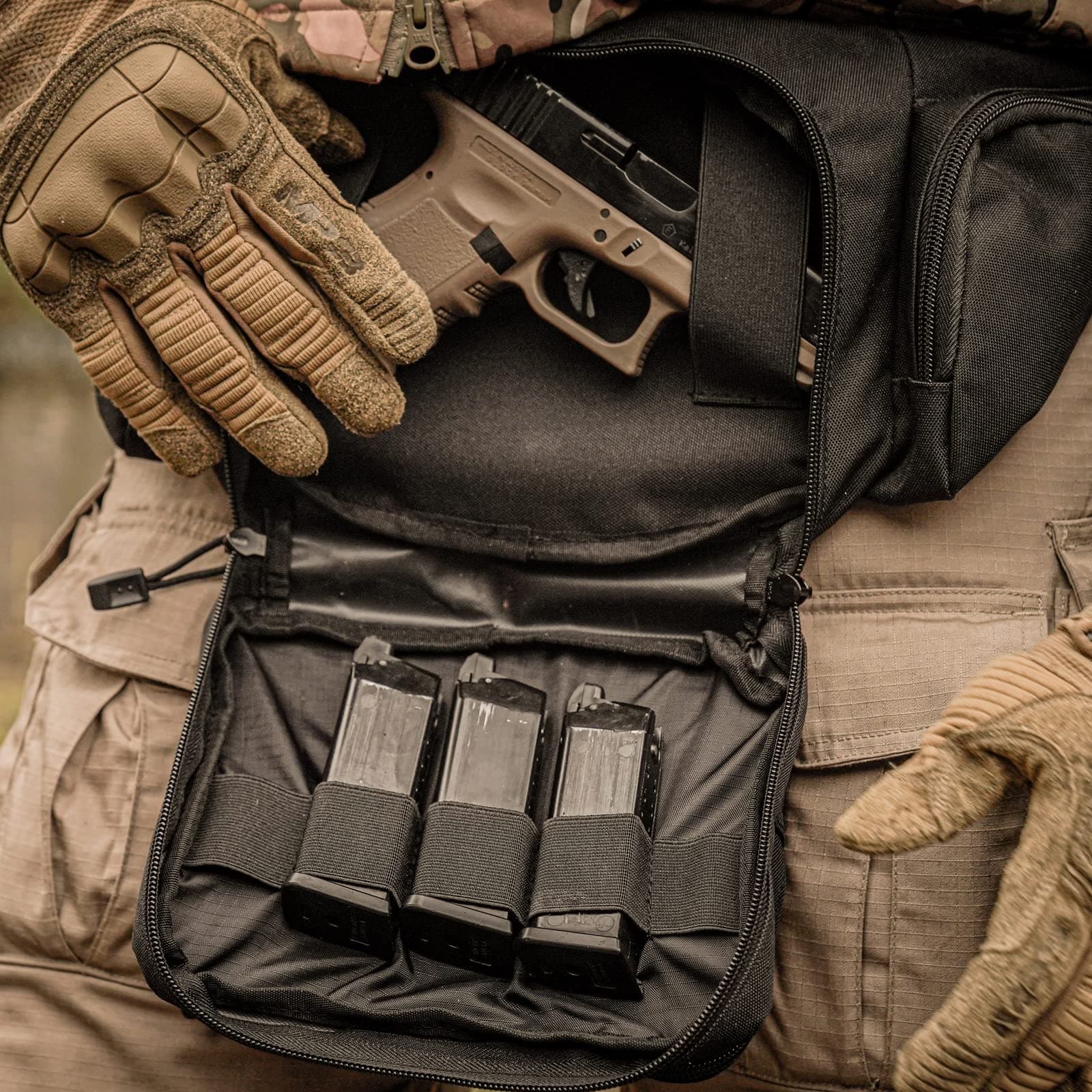 Gloved hands holding a tan handgun and three magazines in a black bag, with tactical gear visible.