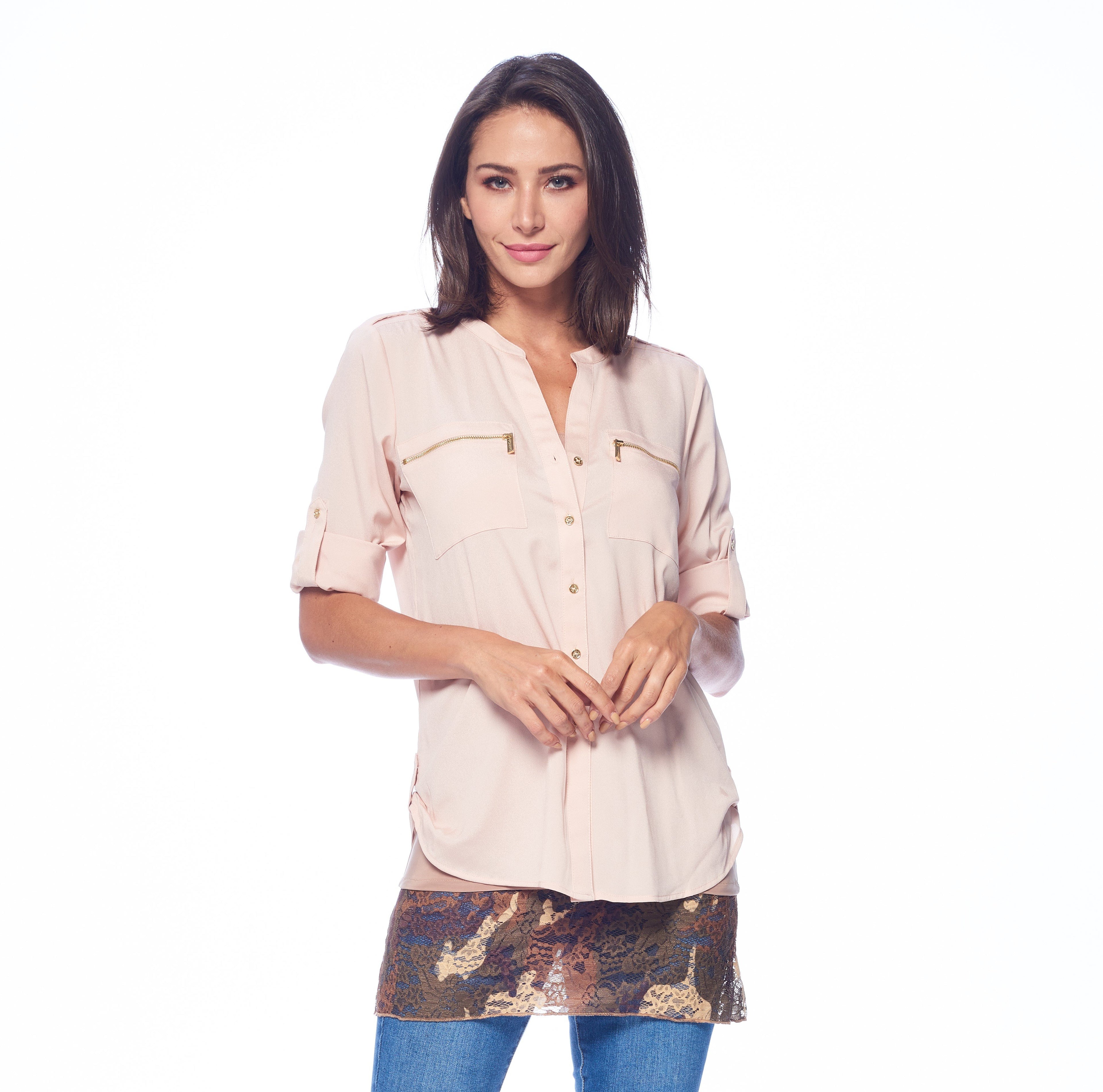 Woman in light pink blouse and blue jeans stands against white background, smiling gently.