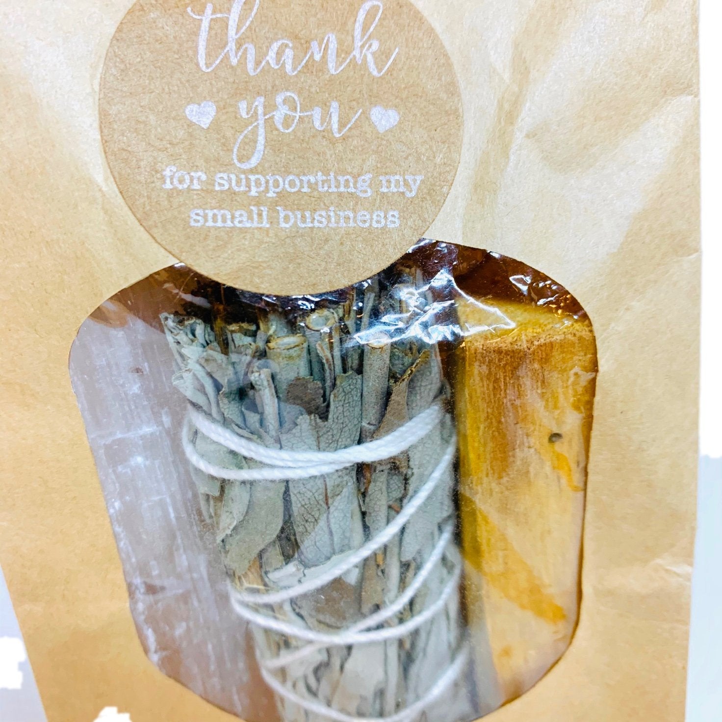 A sage bundle and palo santo wood in a brown paper bag with "Thank you" label.