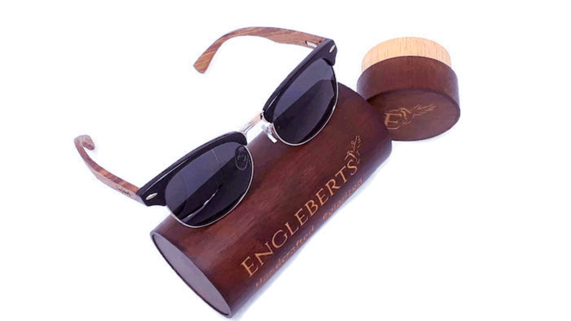 Dark sunglasses with wooden arms on a wooden engraved case, angled view.