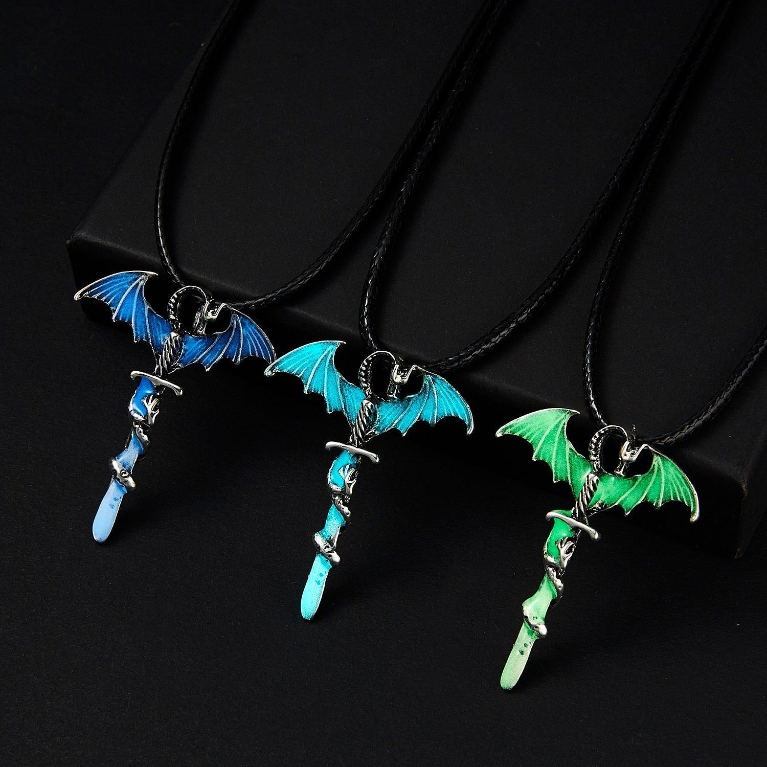 Three necklaces with dragon-wing pendants in blue, teal, and green, on black background.