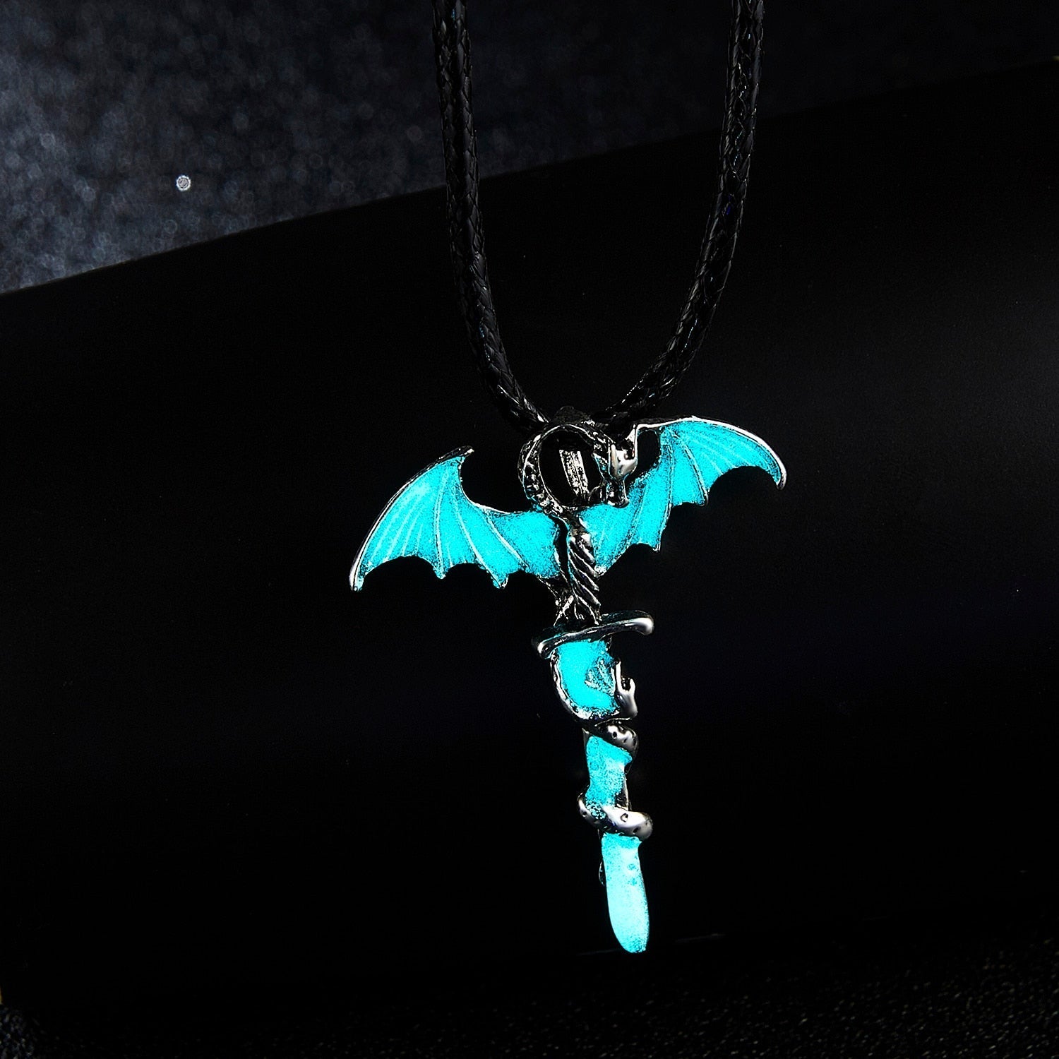 Pendant with blue dragon wings and snake wrapped around a sword, on a black background.
