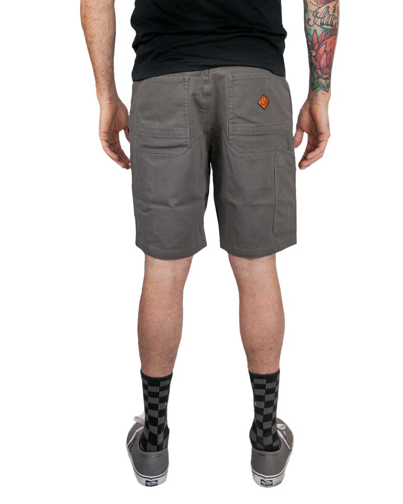 Man in gray shorts from behind, tattoos on left arm, checkered socks, and gray shoes.