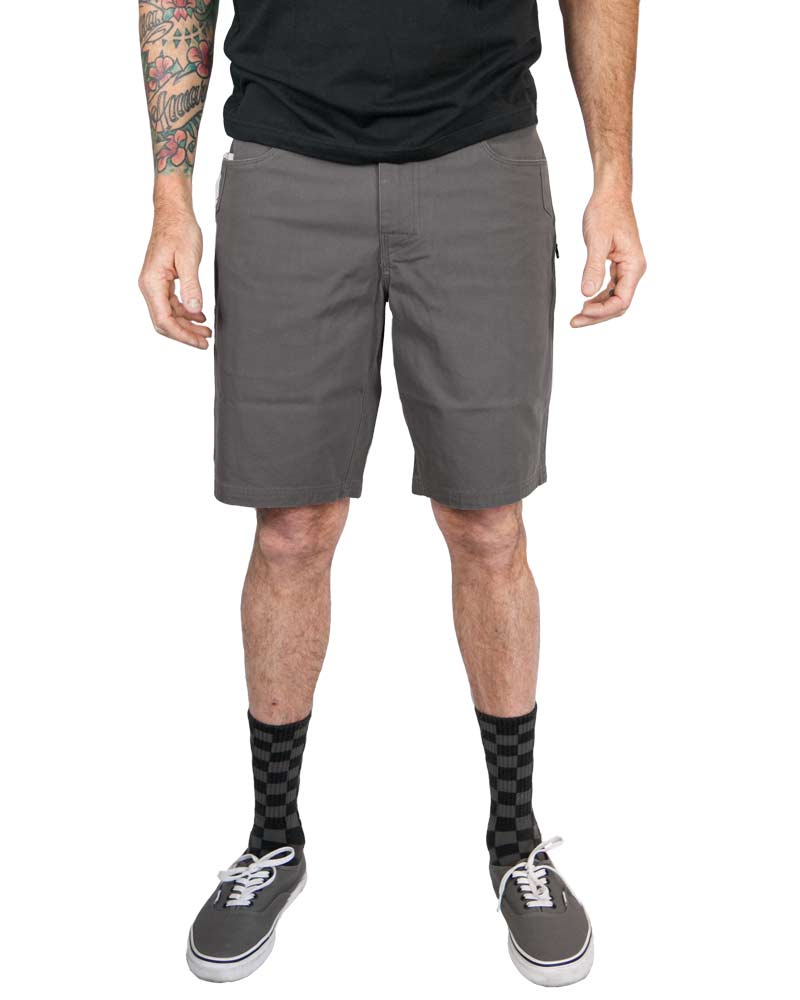 Man wearing gray shorts, black socks, gray sneakers, black shirt, with tattooed arms.