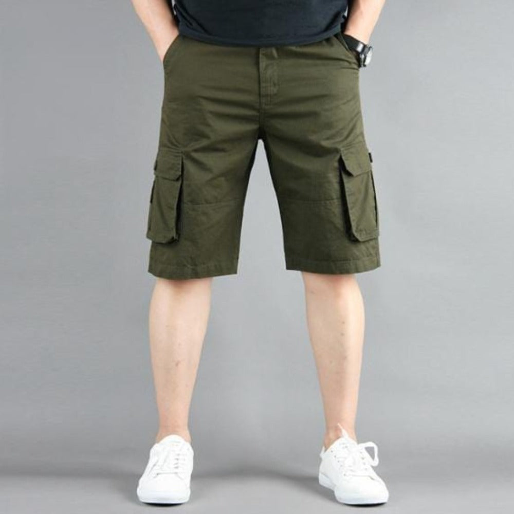Man in olive cargo shorts and white sneakers against a gray background.
