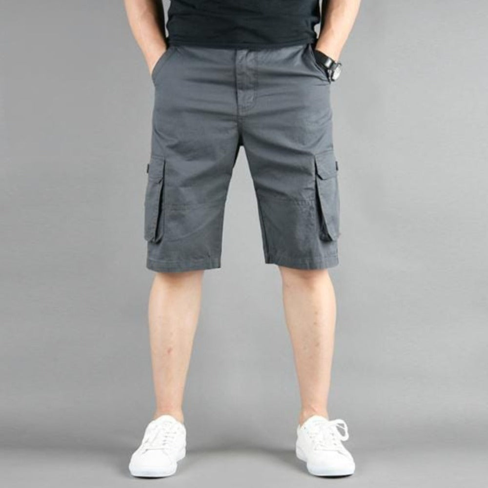 Man in gray cargo shorts and white sneakers against a gray background.