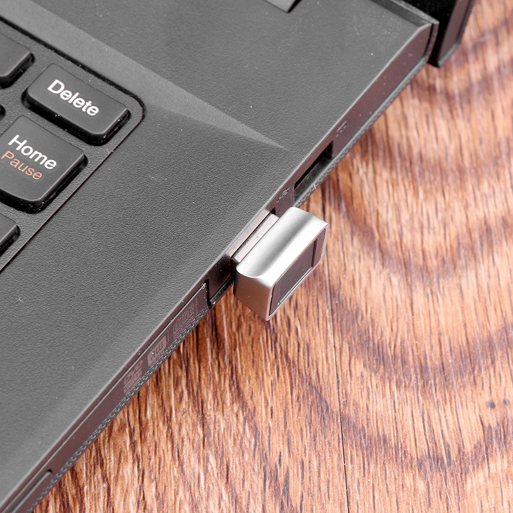 USB device plugged into a laptop on a wooden surface, near keyboard keys "Delete" and "Home".