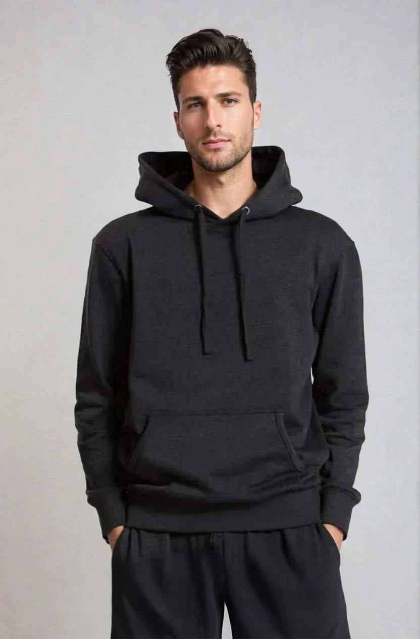 Man wearing a dark hoodie and pants, hands in pockets, against a light gray background.