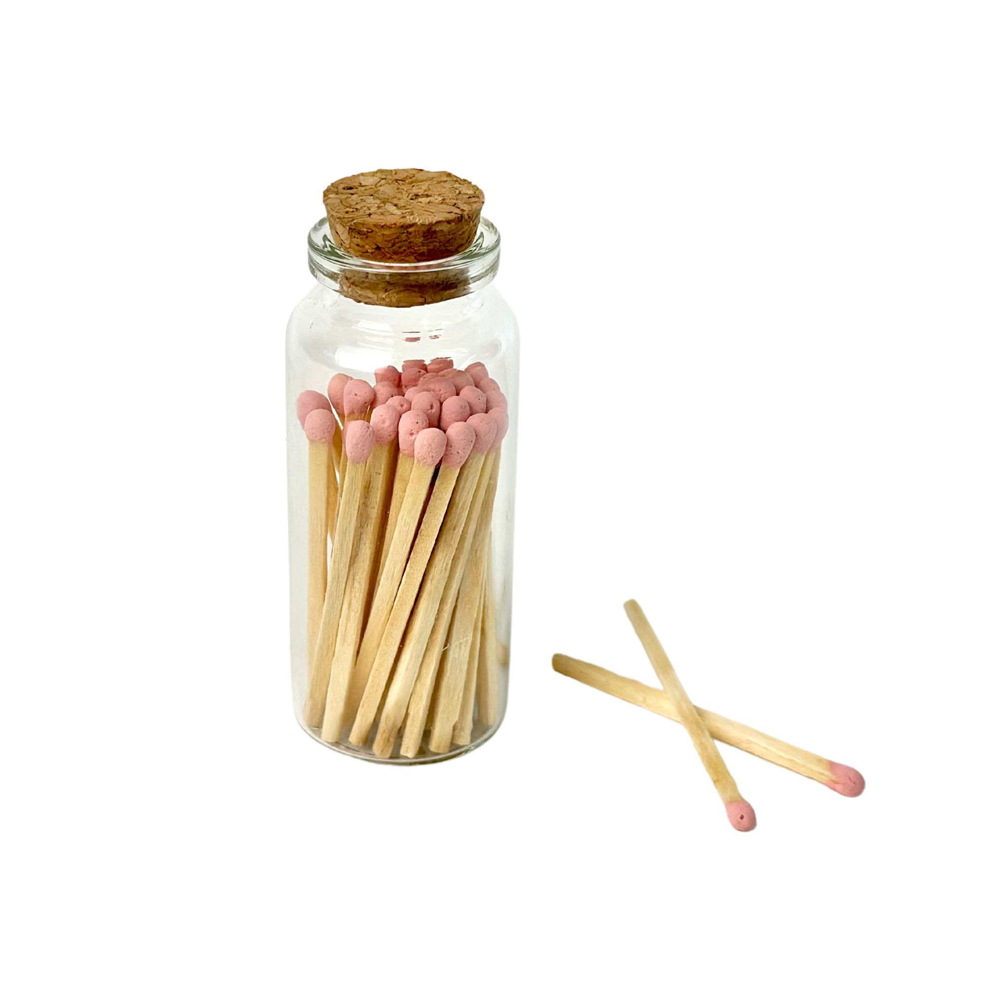 Glass jar with cork filled with matches, pink tips; two matches lie beside it.