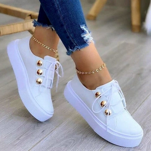 White platform sneakers with gold studs, worn with ripped blue jeans and gold anklets.