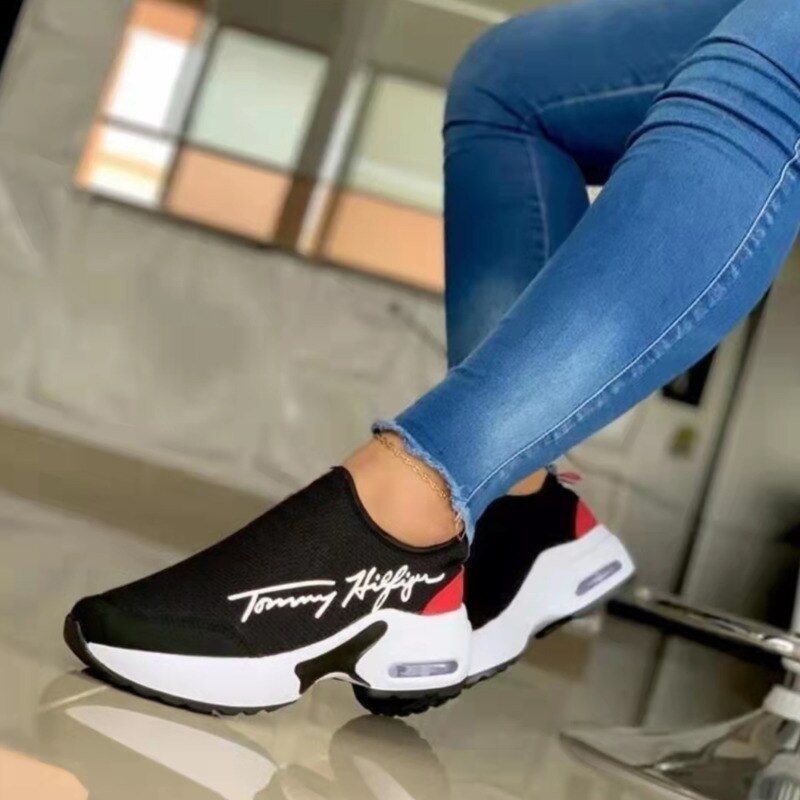 Black and white slip-on sneakers with red accents, worn with blue jeans.