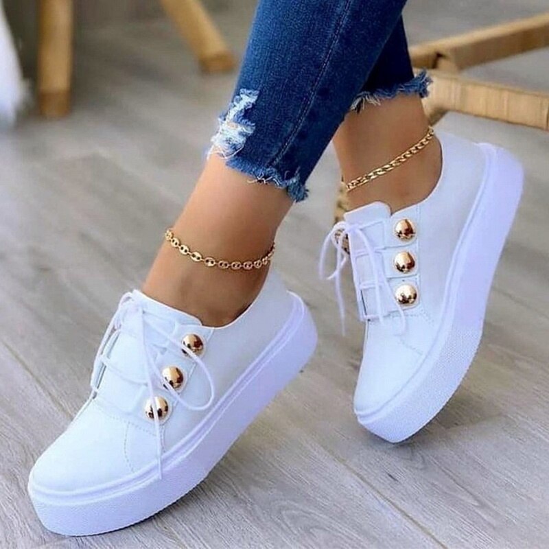 White platform sneakers with gold accents worn with ripped blue jeans and a gold anklet.