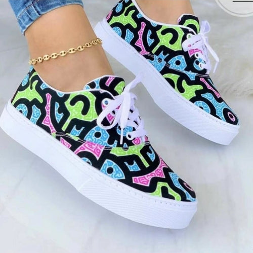 Colorful sneakers with abstract patterns in green, blue, and pink over black, with white soles and laces.