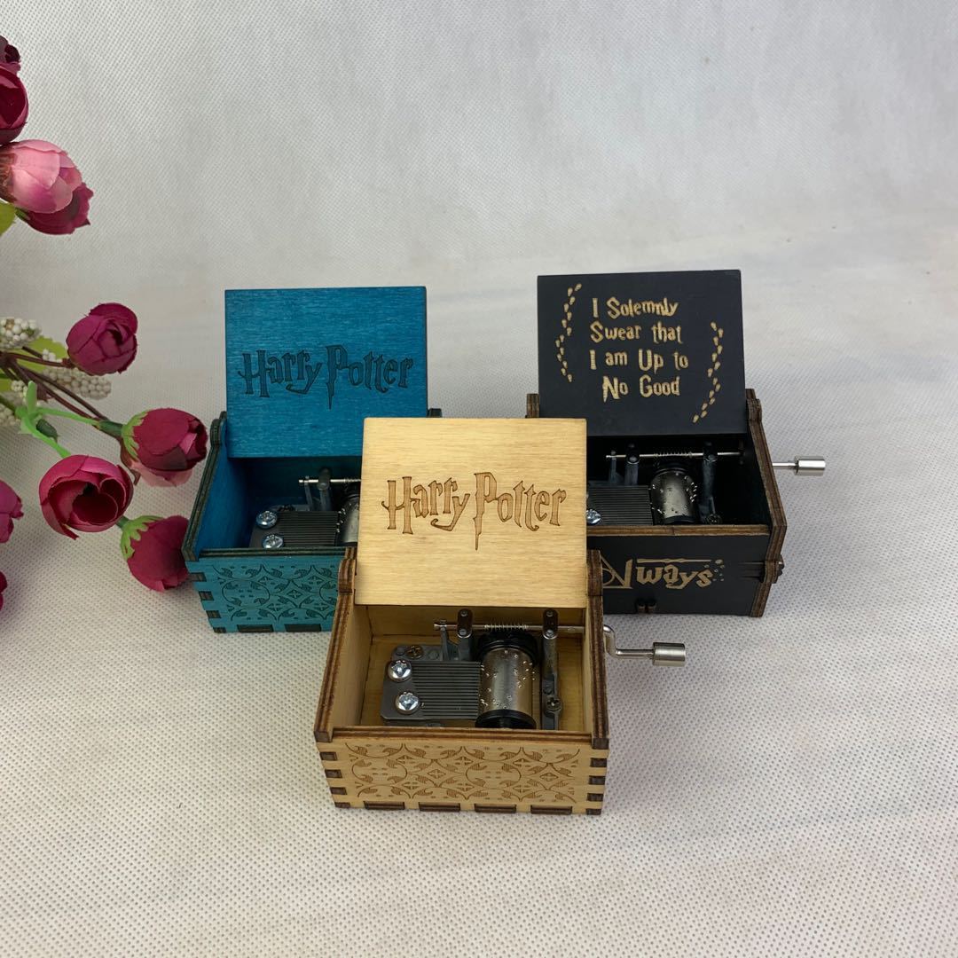 Three engraved wooden music boxes with "Harry Potter" themes, surrounded by pink flowers.