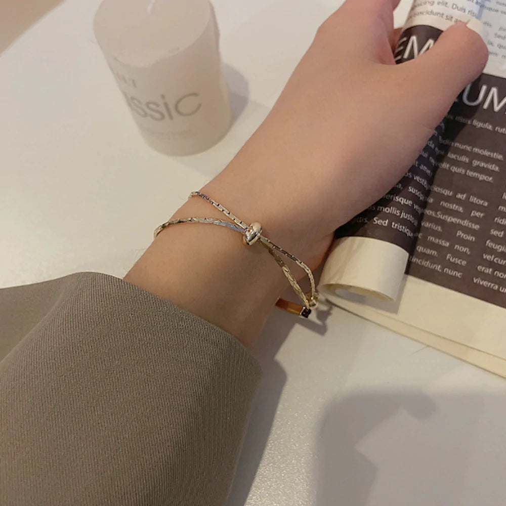 A hand with a gold bracelet rests on a table, holding a rolled-up magazine.