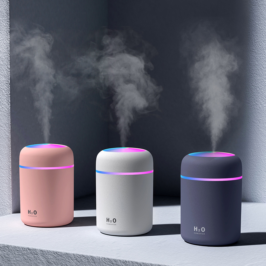 Three colorful humidifiers with LED lights emit mist against a dark background.