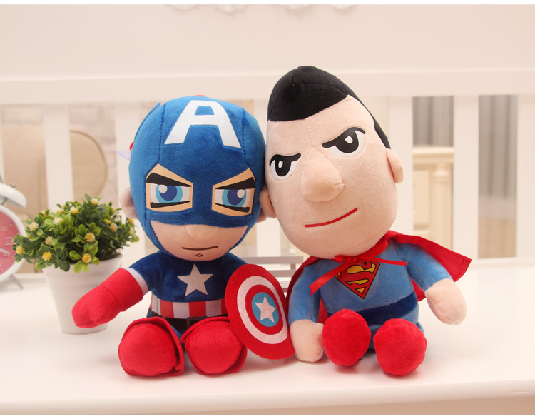 Two plush toys of superheroes in blue suits and red accents, sitting on a white surface.