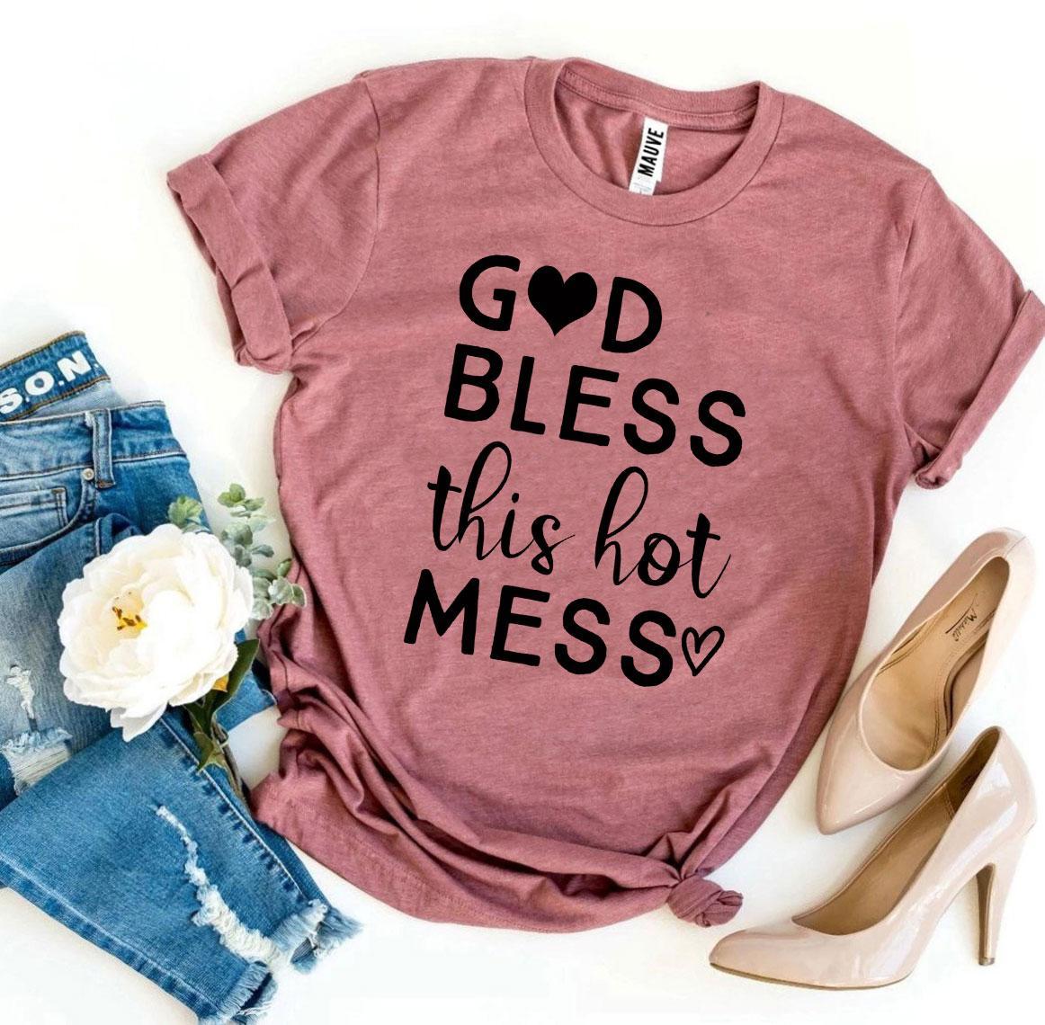 Pink T-shirt with "God Bless This Hot Mess" in black text, paired with jeans, heels, and a white flower.