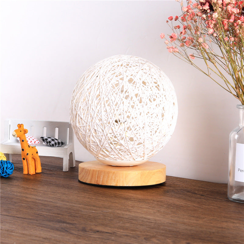 White yarn ball lamp on wooden base, next to orange giraffe figurine and pink flowers in a vase.
