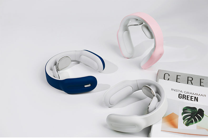 Three neck massagers in navy, pink, and white next to a magazine on a white surface.