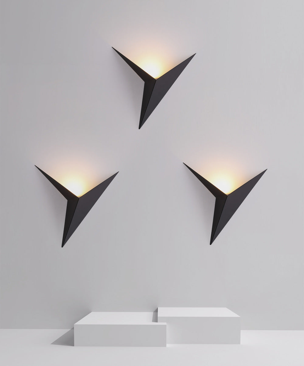 Three black triangular wall lights on a white wall with soft yellow glow, above white geometric blocks.