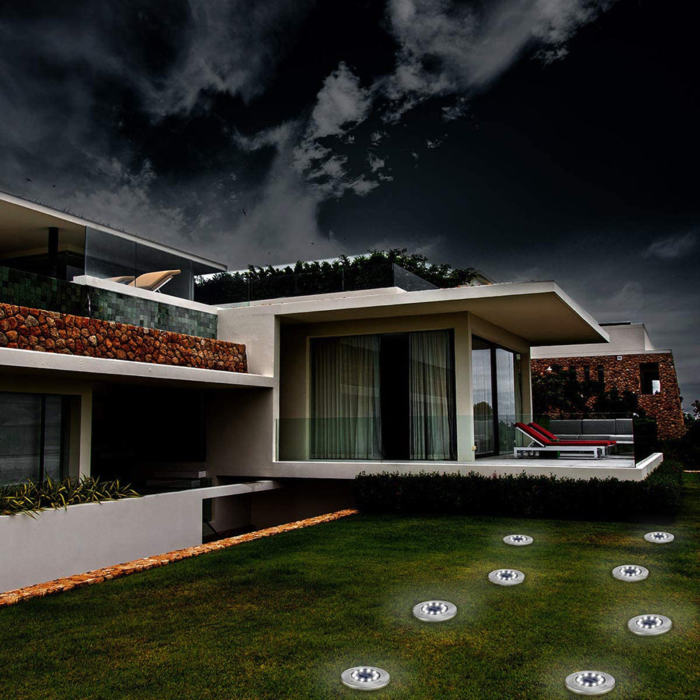 Modern house at night with a flat roof, large glass windows, and ground lights on the lawn.