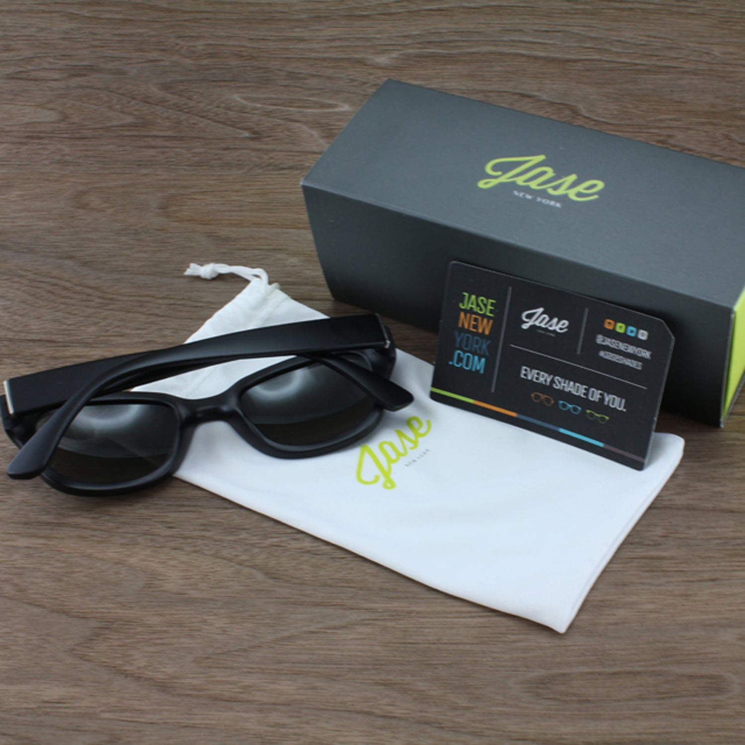 Black glasses with case, box, and card on a wooden surface.