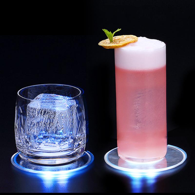 A clear glass with ice and a pink drink with foam, both on glowing blue coasters.