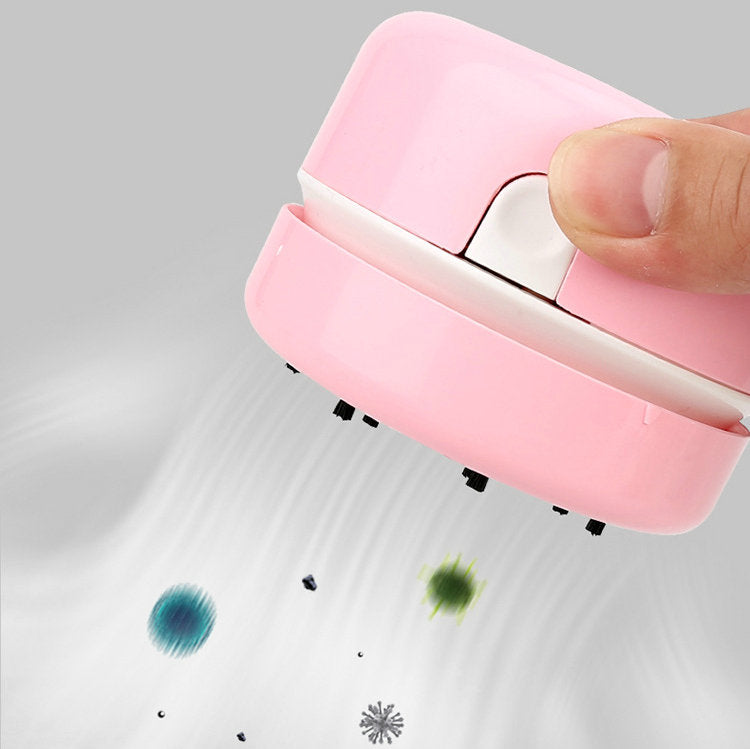 Pink handheld vacuum cleaner removing colorful dust on a gray surface.