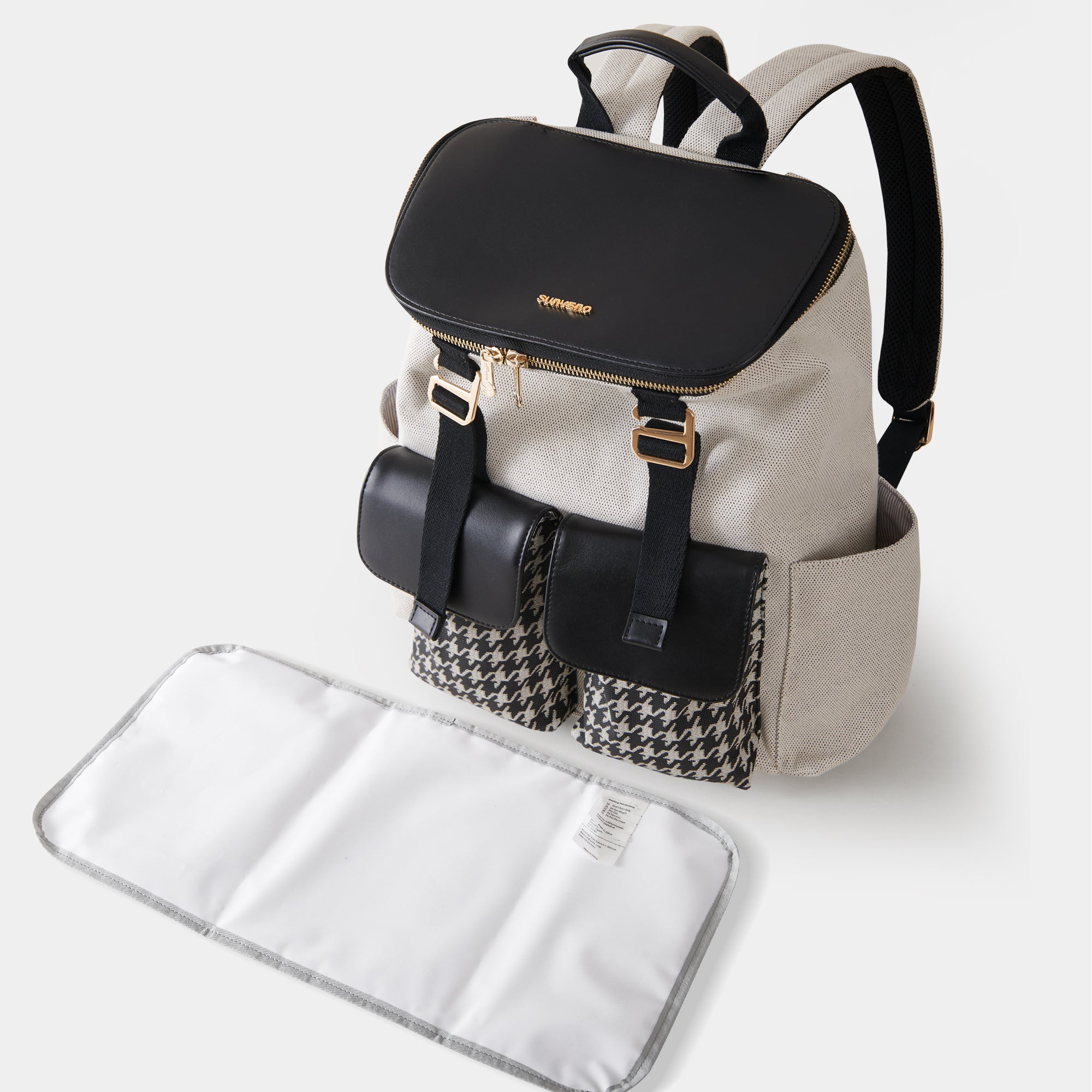 Beige backpack with black flap, gold buckles, houndstooth pockets, and a white changing mat.