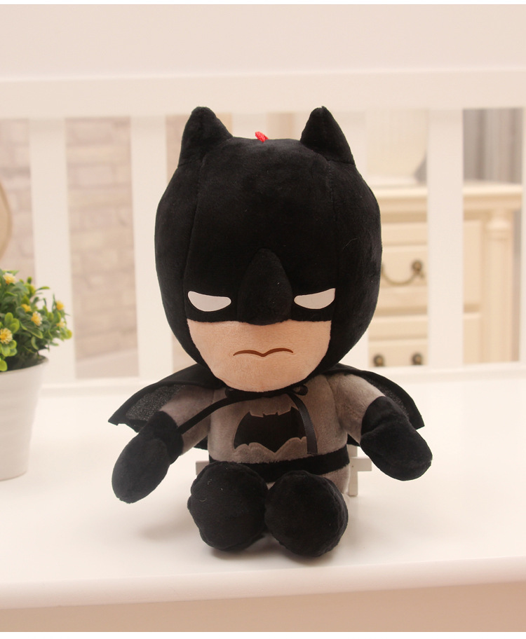 Cute plush toy in black and gray superhero costume, with a stern expression; potted plant nearby.