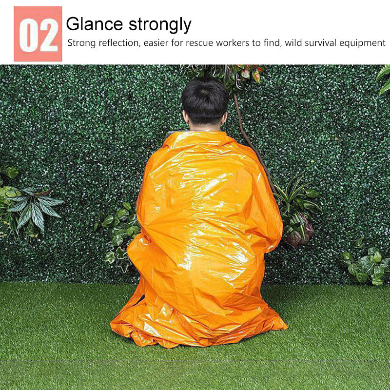 Person in bright orange reflective tarp sits on green grass against leafy hedge background.