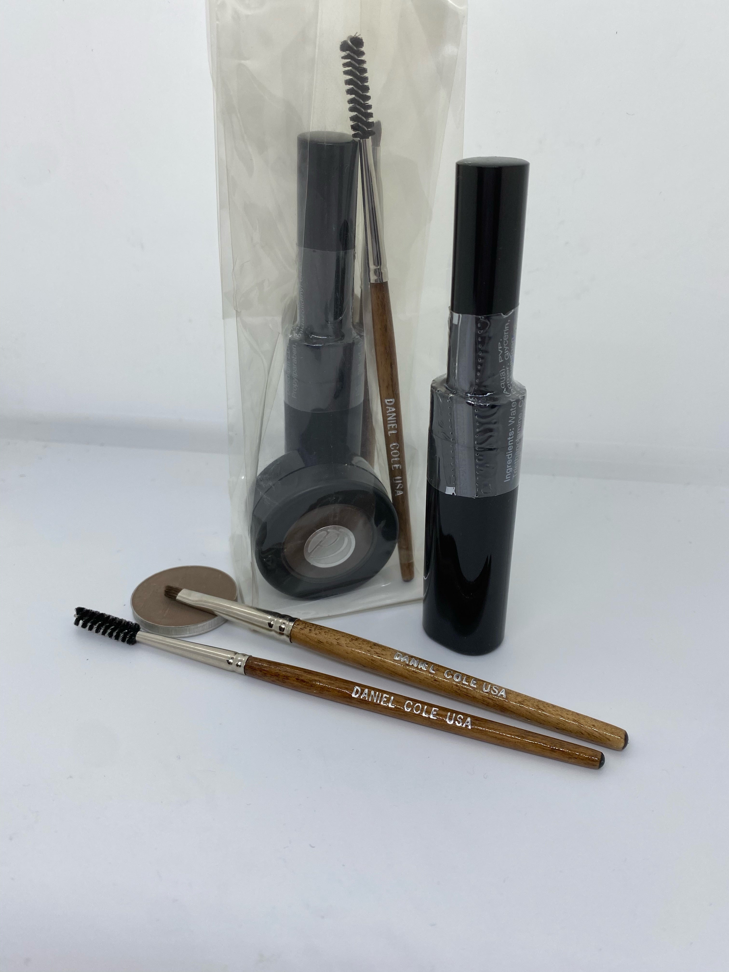 Makeup items with black tubes, two brown-handled brushes, and a round compact on a white background.