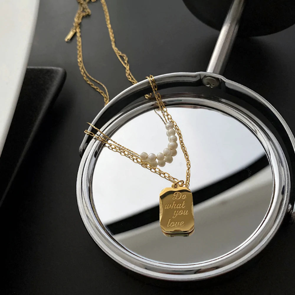 A gold necklace with pearls and a pendant on a small round mirror, reflecting its elegant design.
