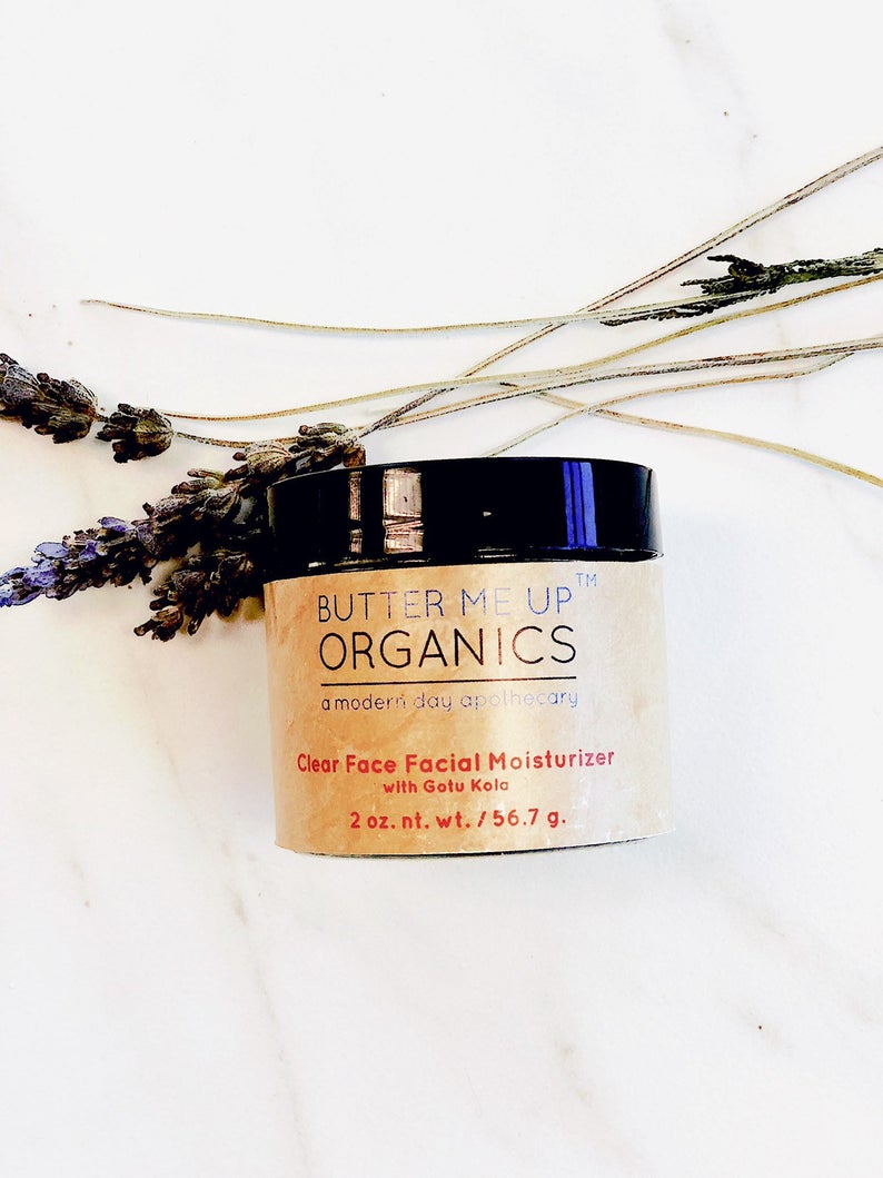 Beige jar of facial moisturizer with black lid on white surface, lavender sprigs beside.