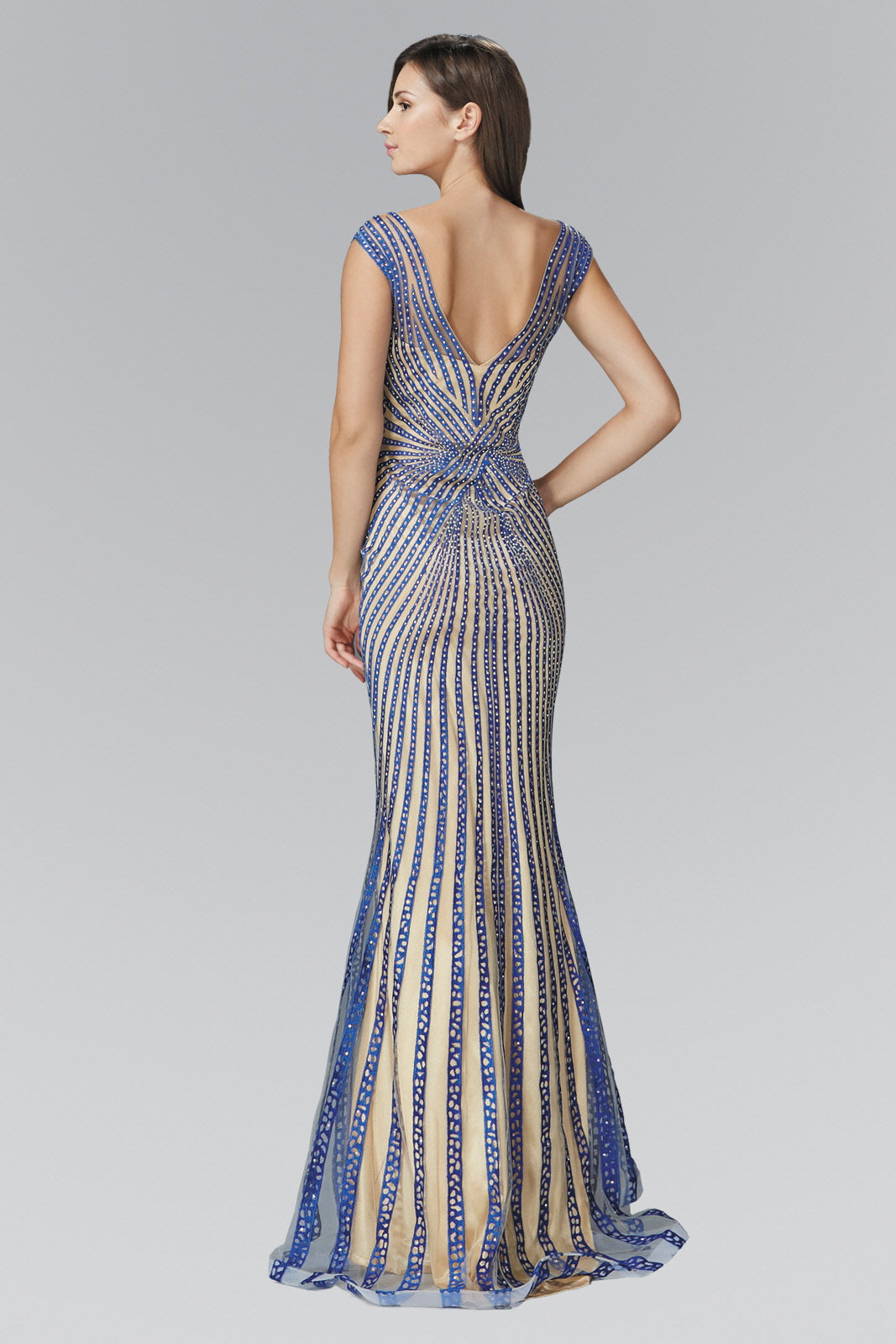 Woman in a blue and beige patterned gown with a deep V-back, standing sideways on a gray background.