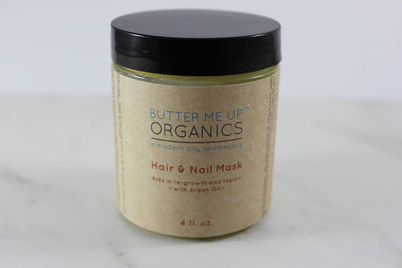 Jar of hair and nail mask with black lid, beige label, blue and red text, on a light surface.
