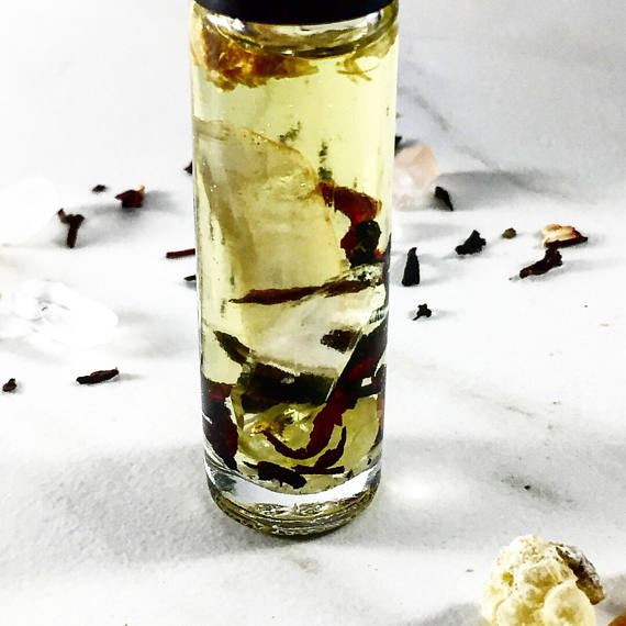 Clear glass bottle with pale yellow liquid, containing herbs, on a white surface with scattered petals.