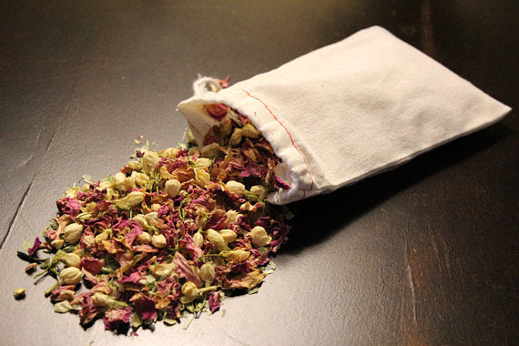White pouch spilling dried colorful flower petals on a dark wooden surface.