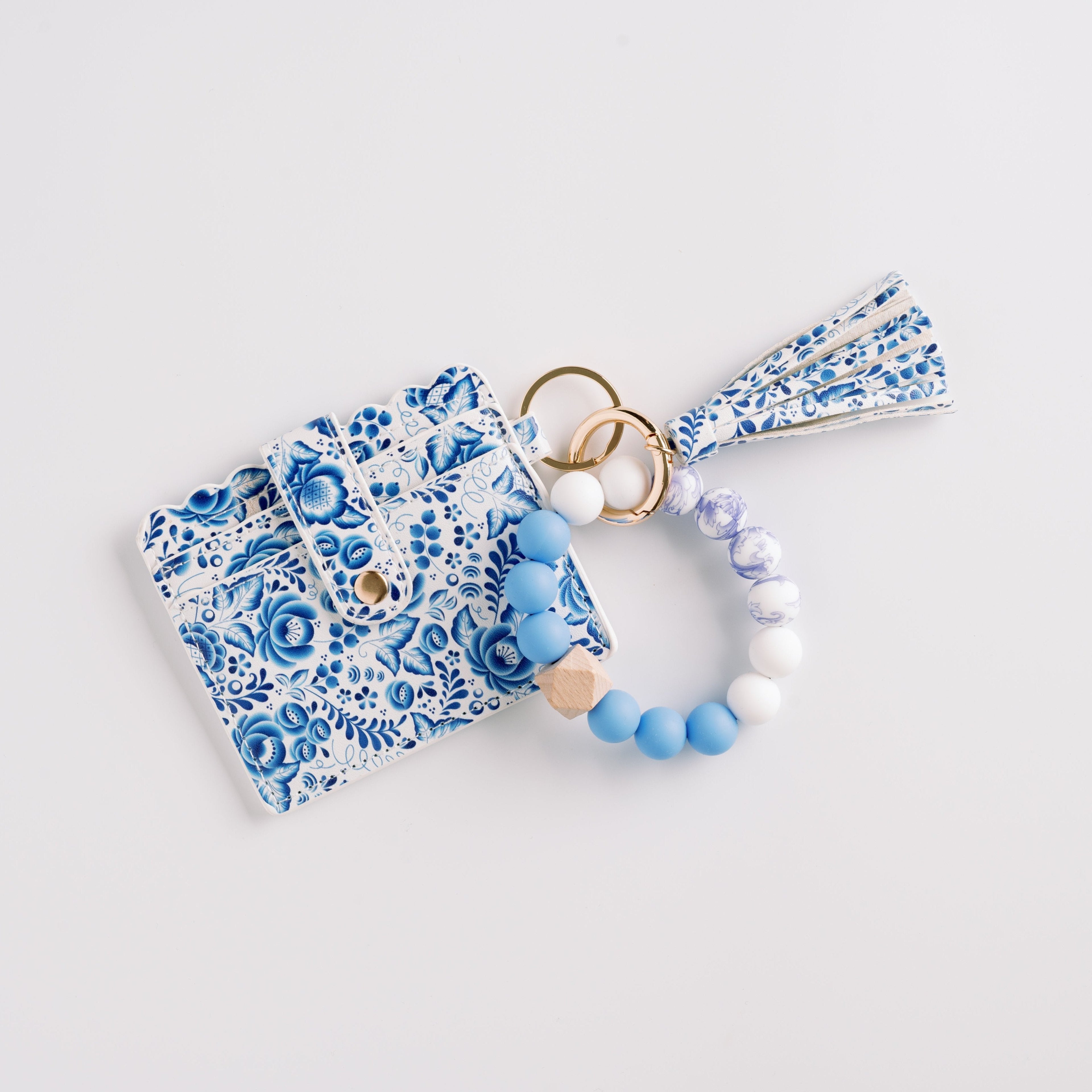 Blue floral cardholder with gold ring and blue-white bead keychain on white background.