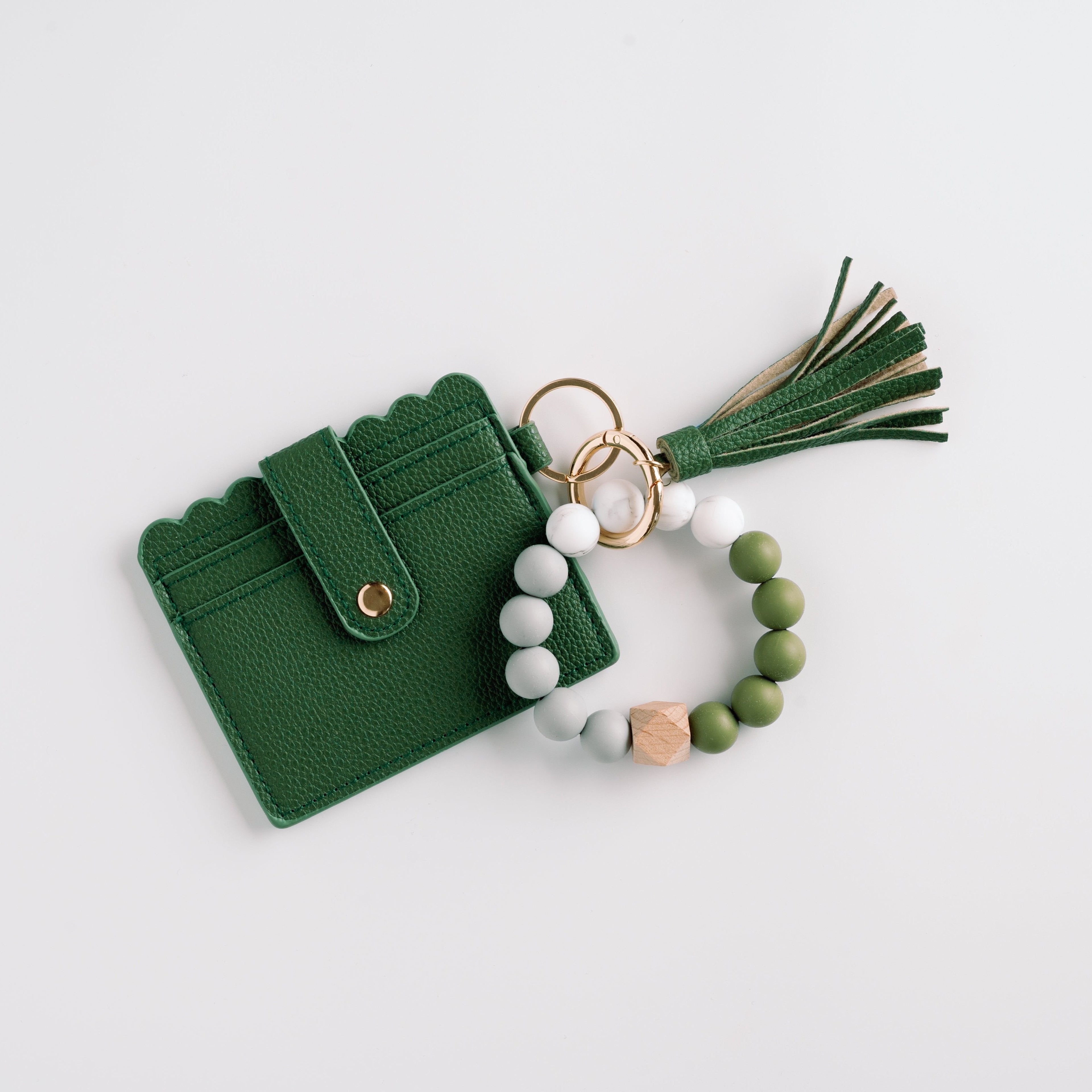 Green wallet with tassel, gold ring, and white-green beaded keychain on a white background.
